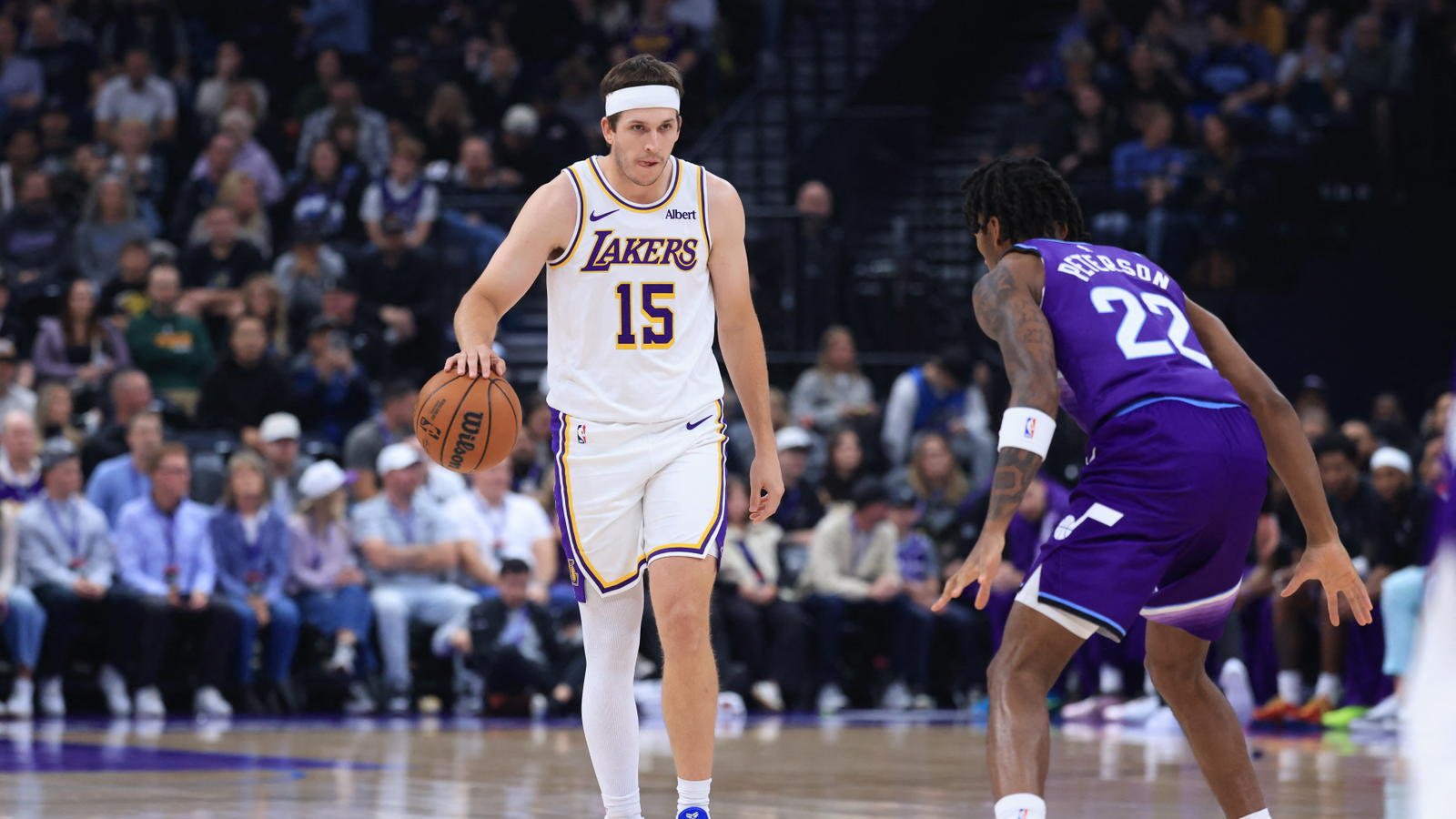 Austin Reaves dribbles up the floor in a white Lakers No. 15 jersey while a Utah Jazz defender in purple waits.
