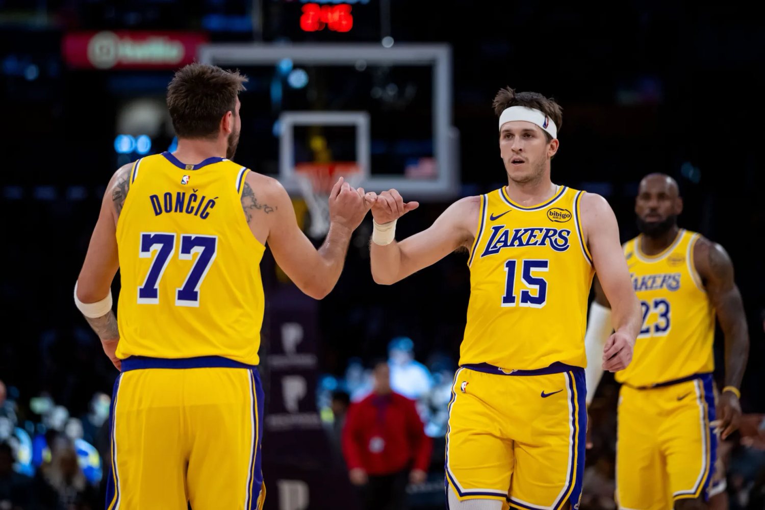 Austin Reaves and Luka Doncic reach toward each other in gold Lakers uniforms.