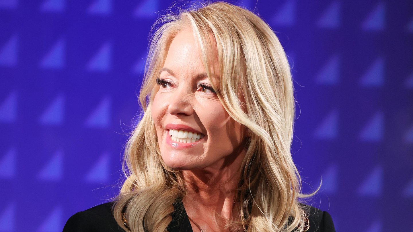 Jeanie Buss smiles and looks off to the side in front of a purple backdrop.