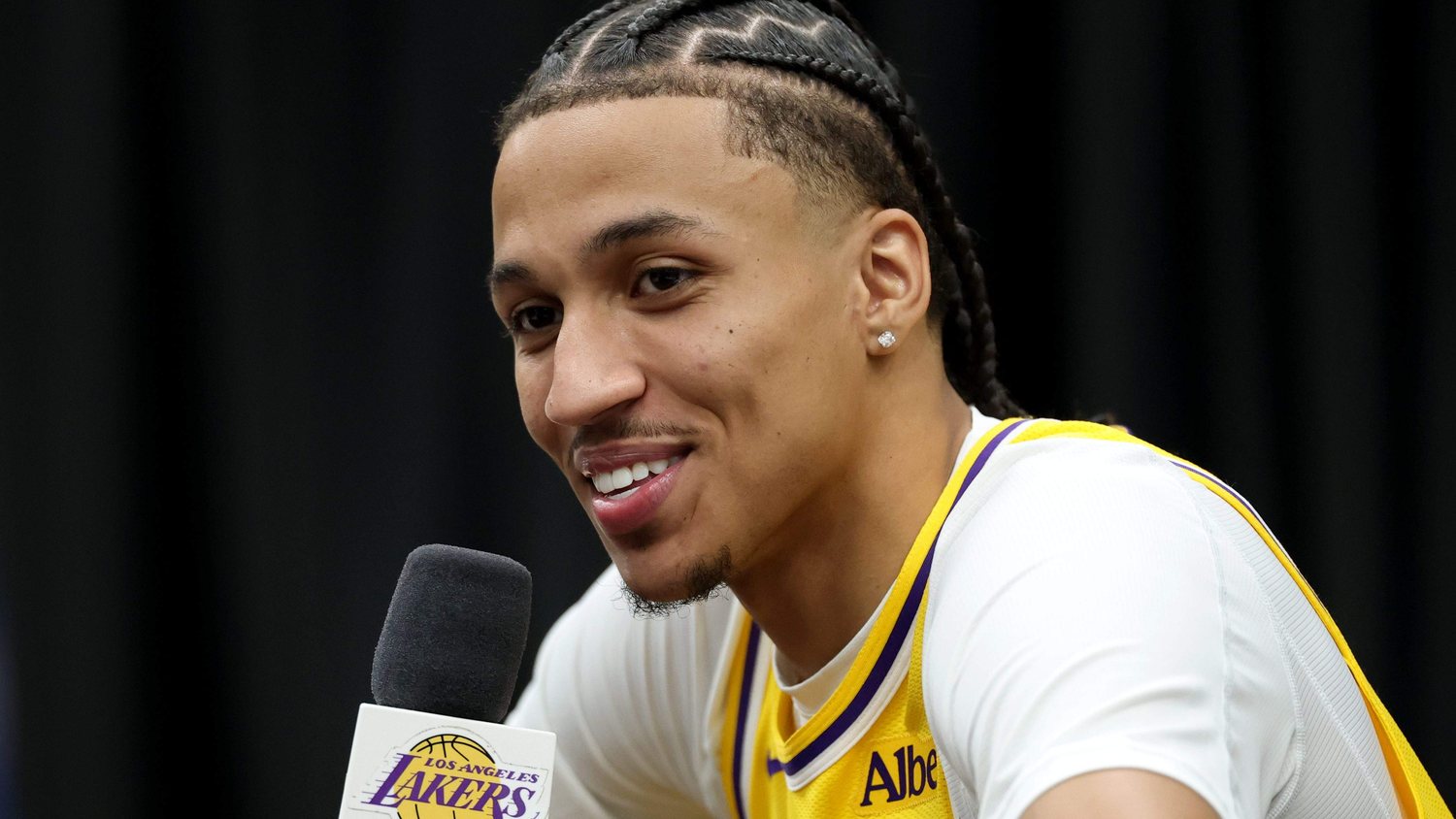 Cameron Carr smiles while speaking into a microphone in a gold Lakers jersey.