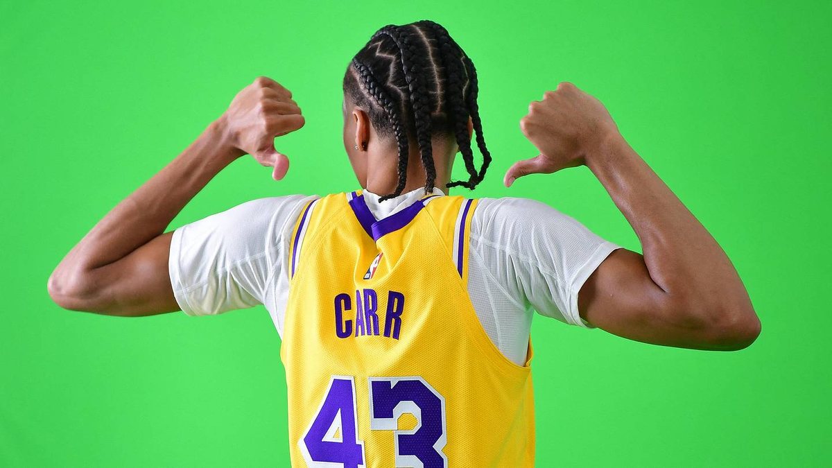 Cameron Carr points toward the name on the back of his gold Lakers jersey against a green background.