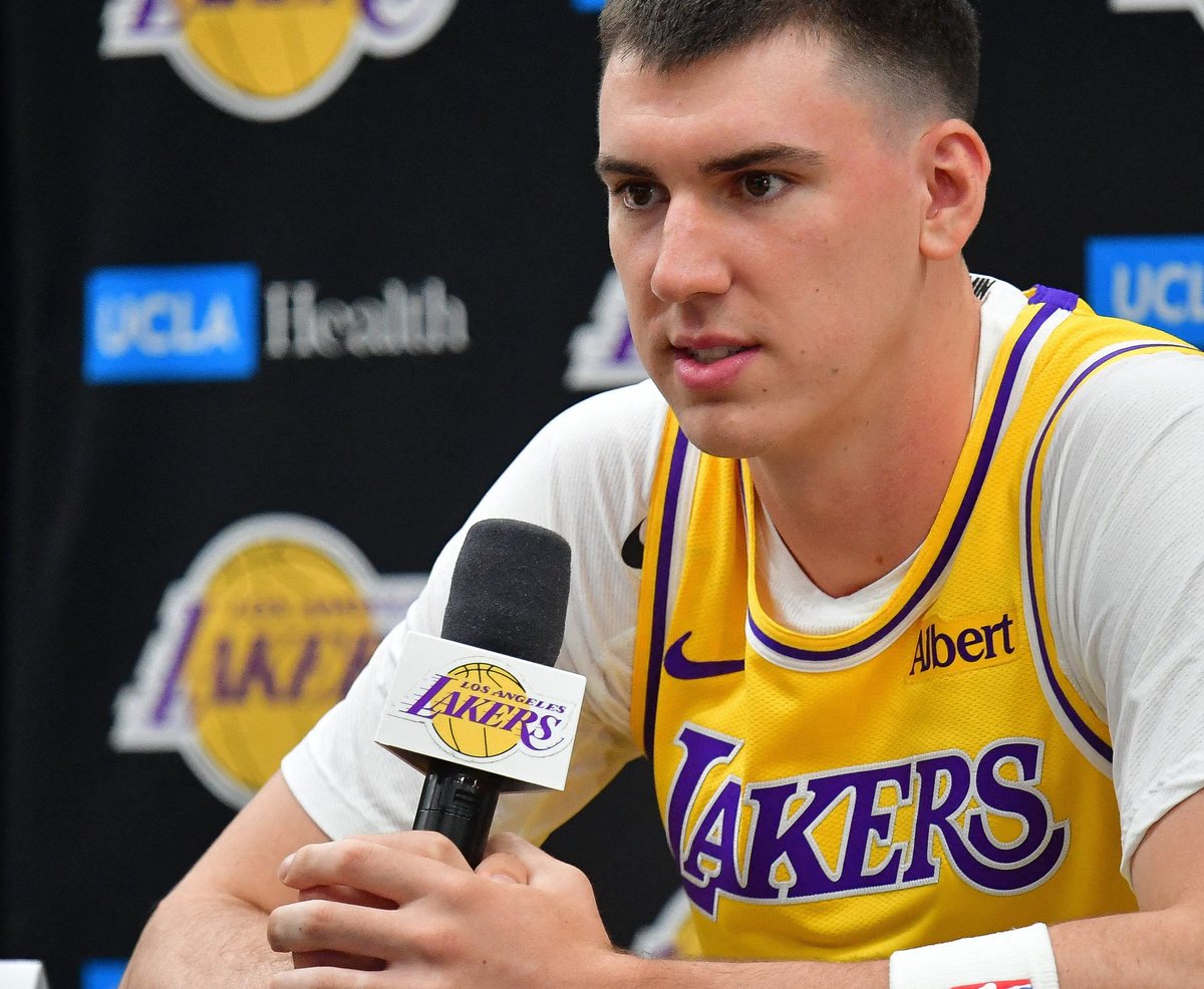 Jake LaRavia, in a gold Lakers jersey, speaks into a microphone at a press conference.