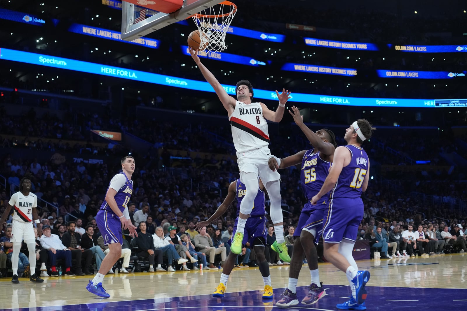 Deni Avdija, in a white Blazers No. 8 jersey, rises for a layup as Kevon Looney (No. 55) and Austin Reaves (No. 15) of the Lakers contest in purple.