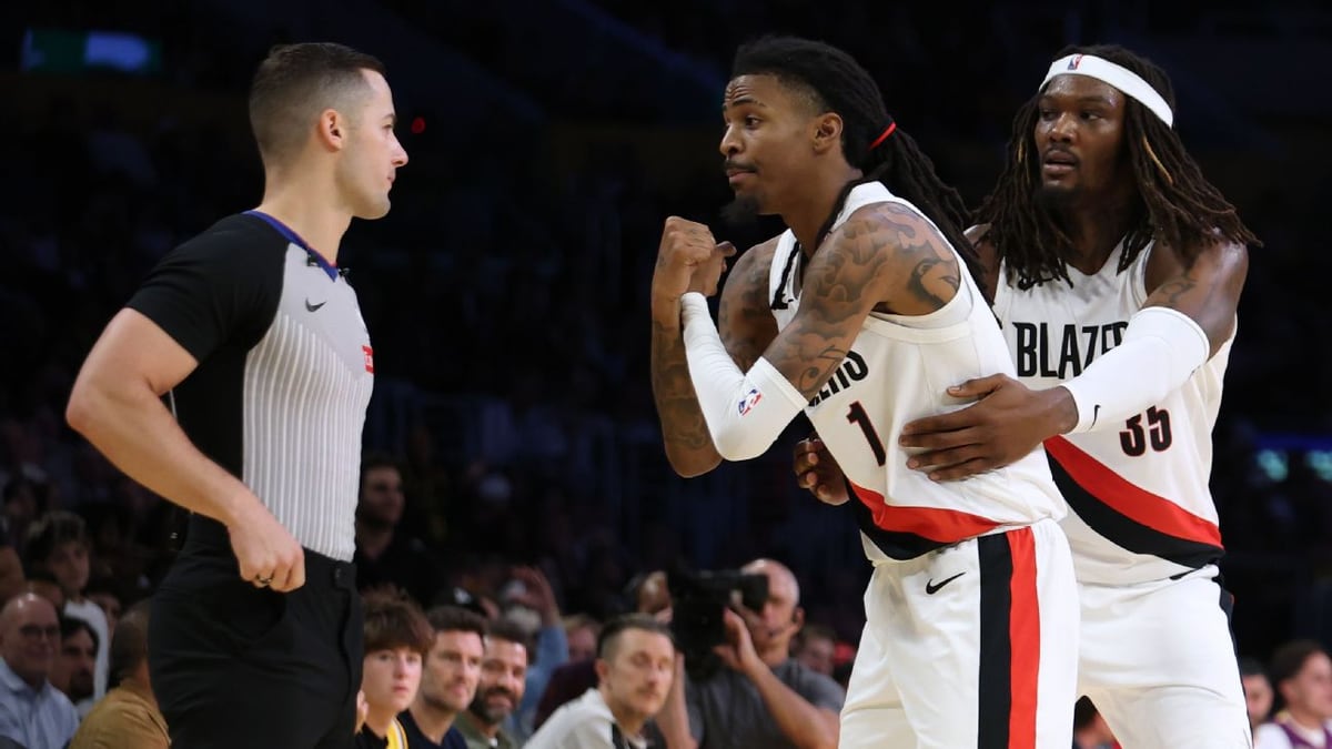 Ja Morant, in a white Blazers No. 1 jersey, faces a referee as teammate Robert Williams III wraps an arm around him.