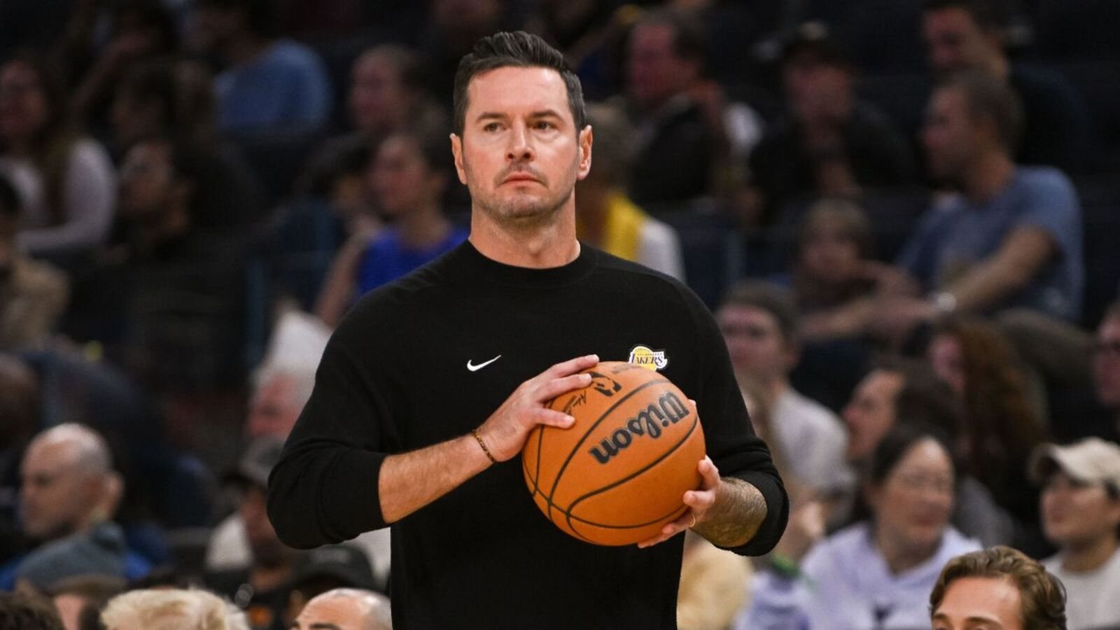 JJ Redick, in a black Lakers pullover, holds a basketball on the court at Chase Center before the preseason game against the Warriors.
