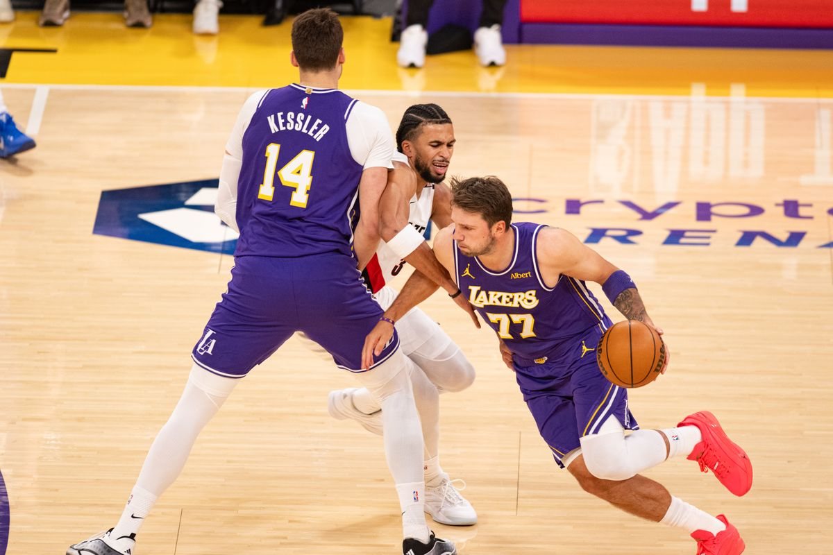 Luka Doncic, in a purple Lakers No. 77 jersey, dribbles around a Walker Kessler screen against a Portland defender.