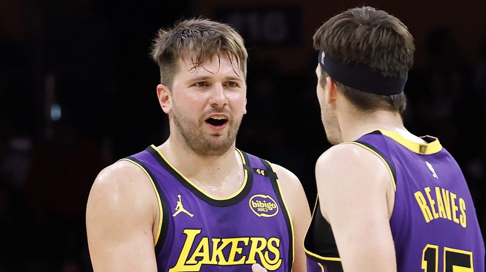 Luka Doncic, in a purple Lakers jersey, talks with Austin Reaves, who has his back to the camera, during a game.